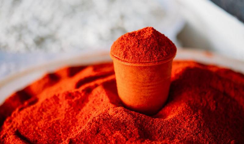 A small cup of cayenne powder atop a larger pile of it.