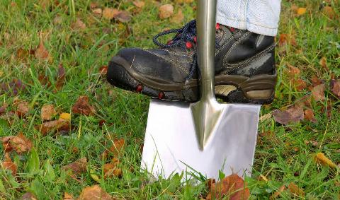 A close photo of someone driving a spade into the ground with their boot.