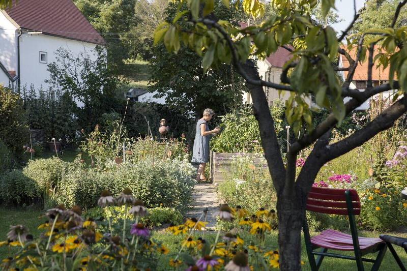 A woman standing in the middle of her large garden, thriving plants surrounding her.