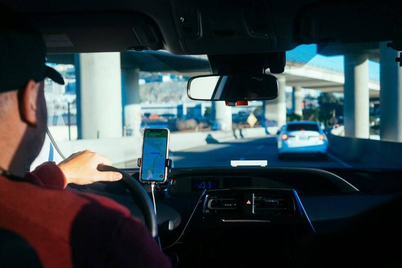 View from the backseat of an Uber vehicle. The driver is staring ahead through the windscreen, with a cellphone propped up next to the steering wheel