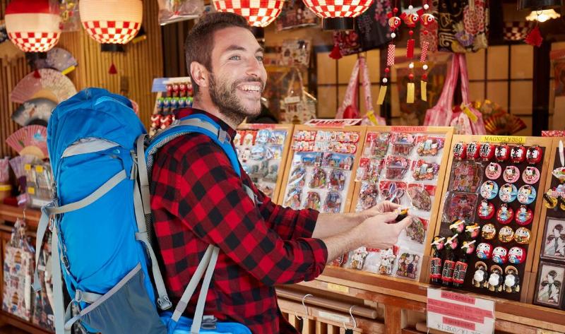 A backpacking tourist smiling while shopping for souvenirs in Japan.