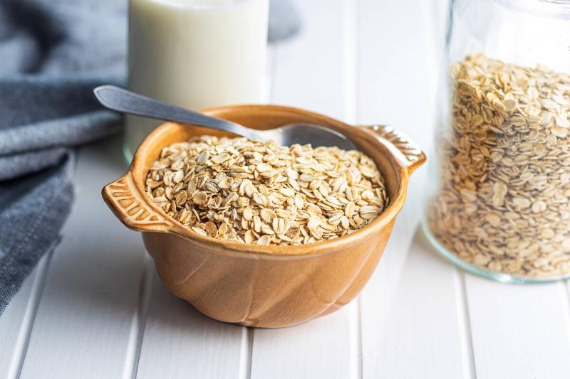 A bowl of rolled oats with a spoon in it next to a jar filled with the rest of the oats.