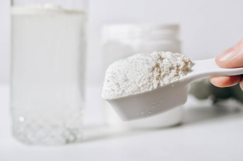 A hand holding a scoop of white powder, powdered milk in this case.