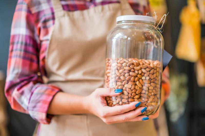 A woman in an apron holding a jar that's mostly filled with a dried bean.