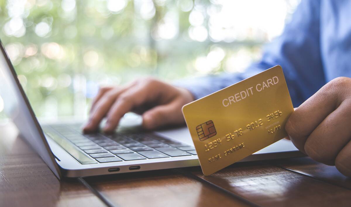 A person holding a credit card next to a laptop.