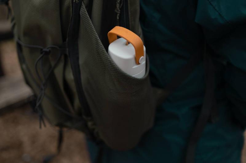 Close up view of young woman with a backpack with thermos in forest. Hiking equipment on footpath in woodland.