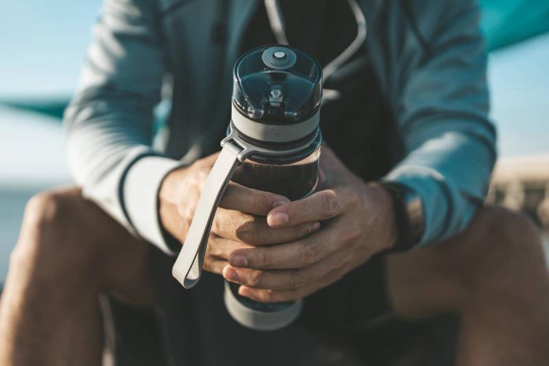 sport man sitting after running and holding water bottle drink. Sport thirsty and resting after exercise.