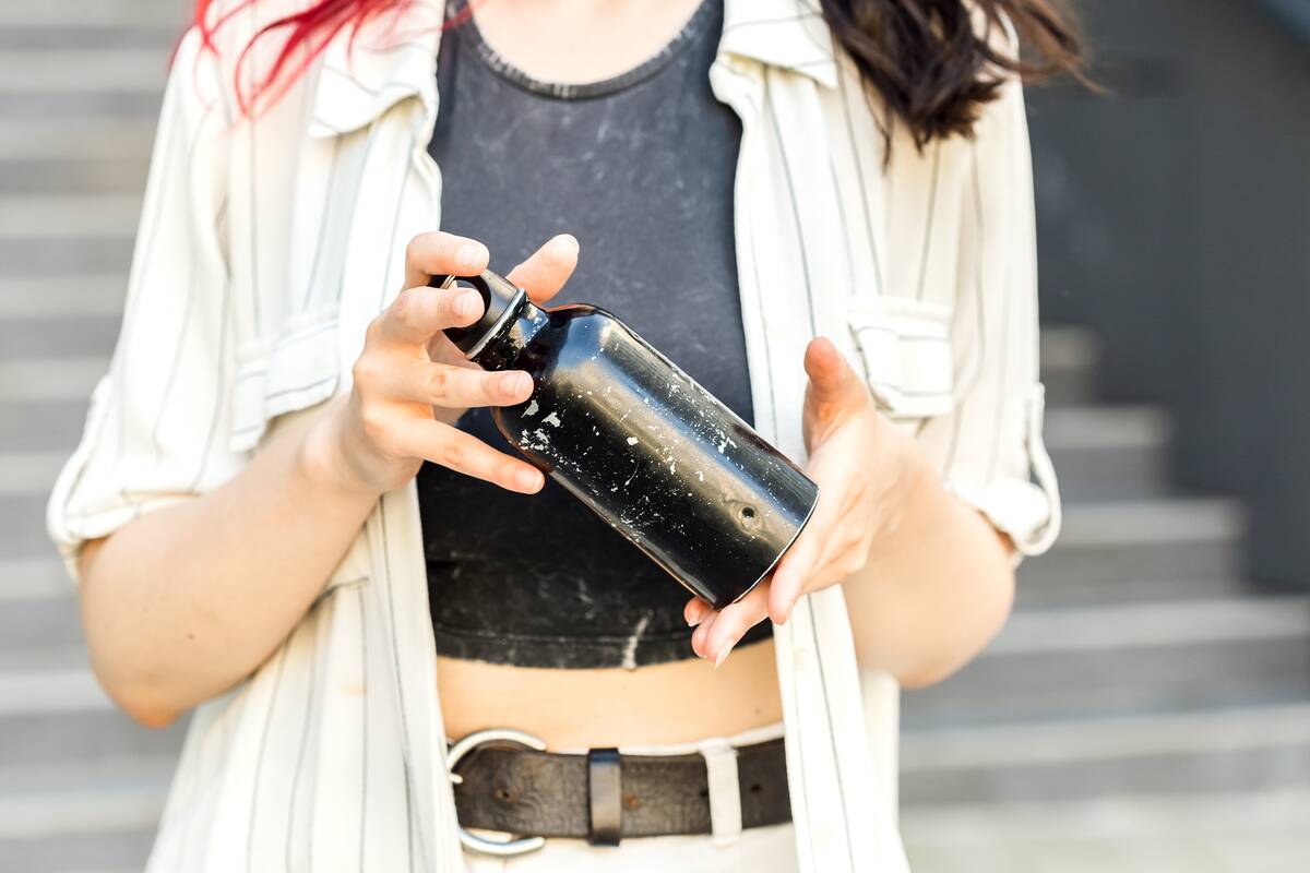Close-up of female hands holding reusable old stainless steel water bottle.
