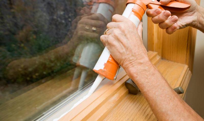 A person applying caulk to a window seal.