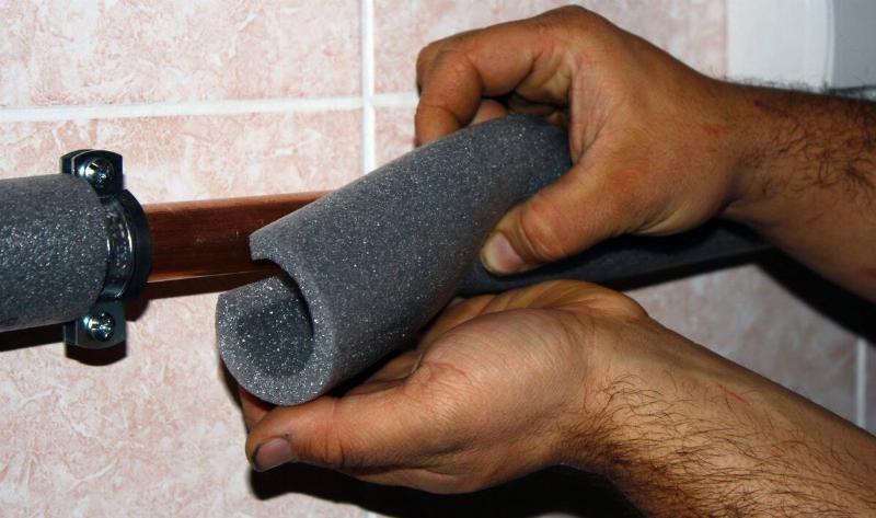 A man's hands installing some pipe-insulating foam.