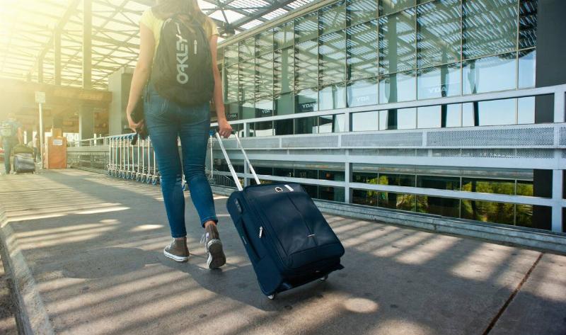 A woman walking outside of an airport, her suitcase in tow.