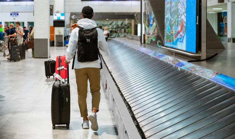 A man walking away from baggage claim with his suitcase in tow.