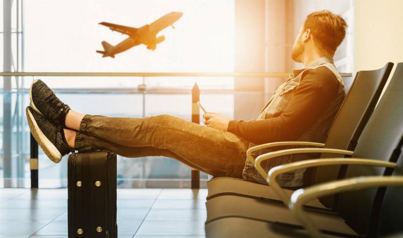 A man lounging in an airport, his feet kicked up on his suitcase.