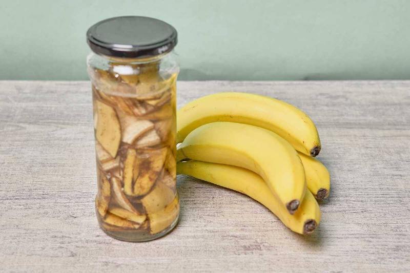 A jar of banana peel water with a bunch of bananas next to it.