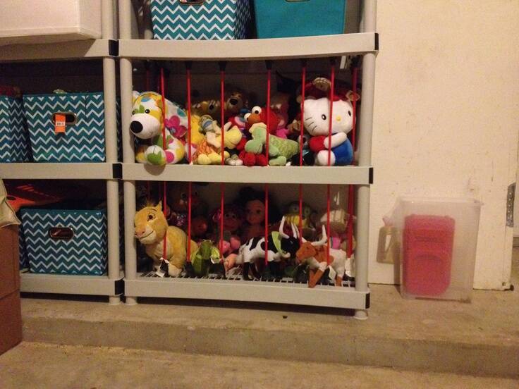 Bungee cords used as bars on an open shelving unit containing plush toys.