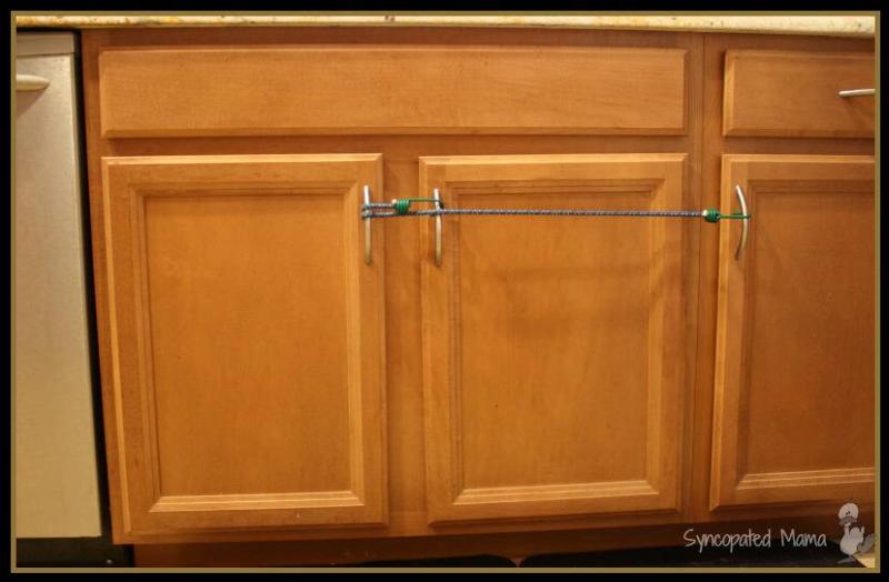 Kitchen cabinet doors being held shut by a bungee cord wrapped through the handles.