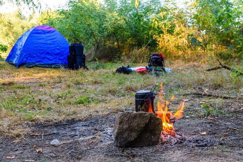 A campsite with a fire going away from the tent, boiling water.