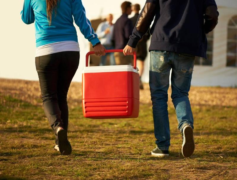 Two people carrying a cooler toward a group of people.
