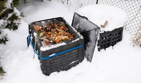 A large compost bin in the water, covered in and surrounded by snow.