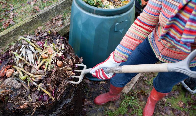 A person sticking a pitchfork into their compost pile, another compost bin next to them.