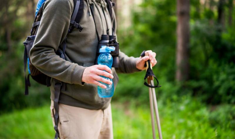 A person hiking in the forest with a water bottle in one hand, walking sticks in the other.