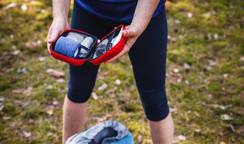 A person holding a small travel first aid kit open in their hands.