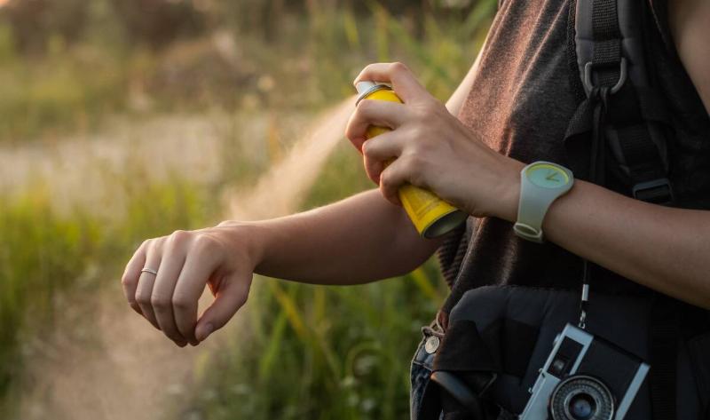 A person spraying bug spray on their arm while outdoors.