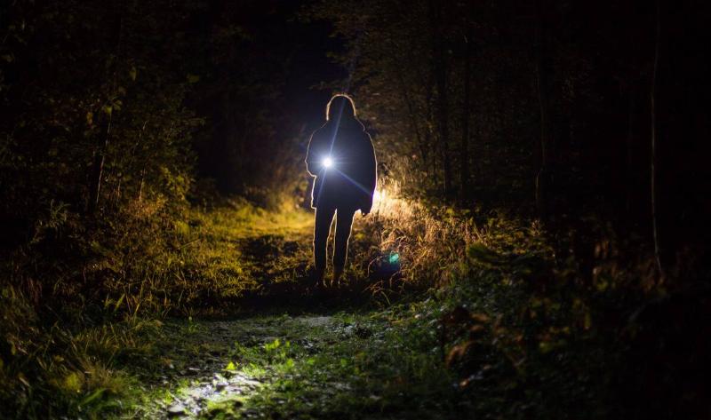 A person standing on a path in the dark, shining a flashlight at the camera.