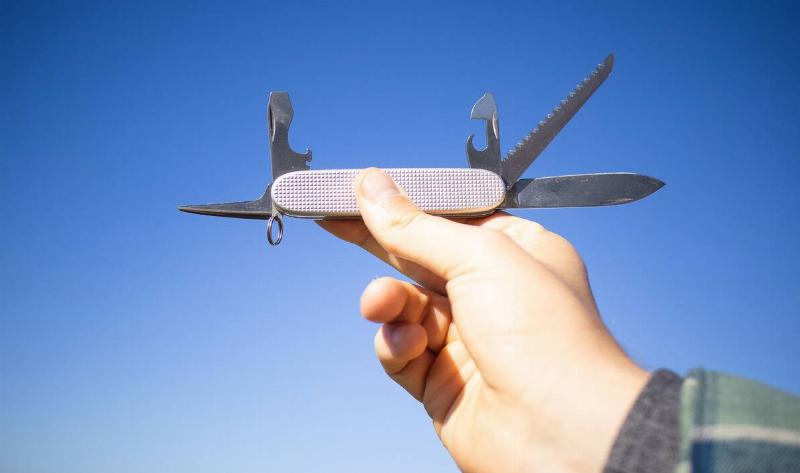 A person holding an opened multi-tool up to the sky.