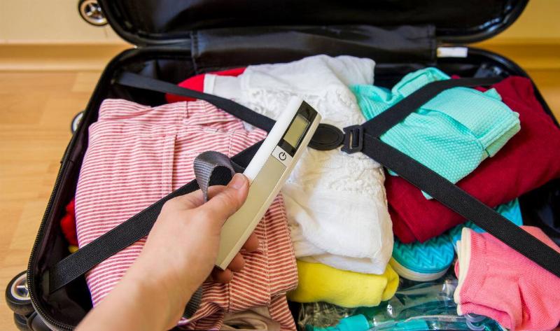 Someone with a full suitcase holding a luggage scale in front of it.