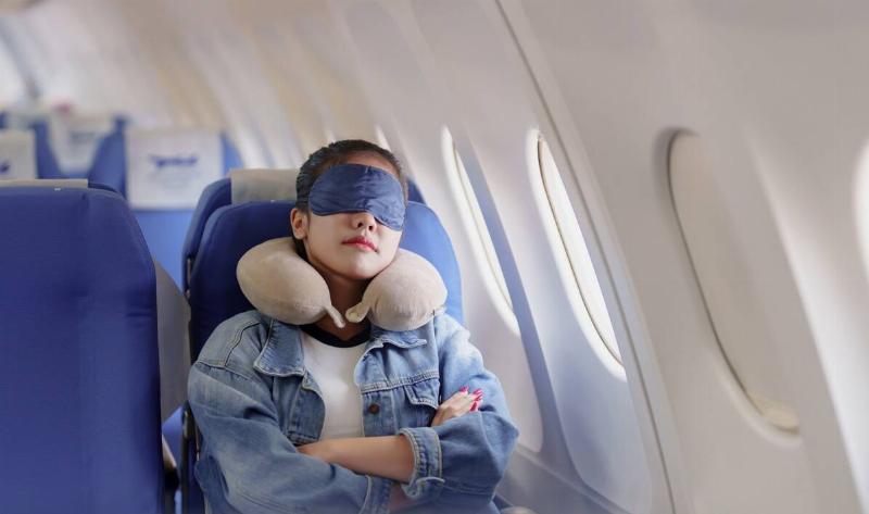 A woman sitting in a plane with an eyemask and neck pillow on.