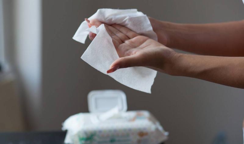 A ppair of hands wiping themselves off with a sanitary wipe, the container in the background.