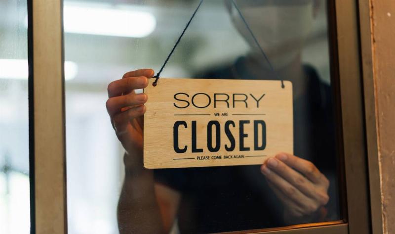 A person putting a 'closed' sign on a store door.