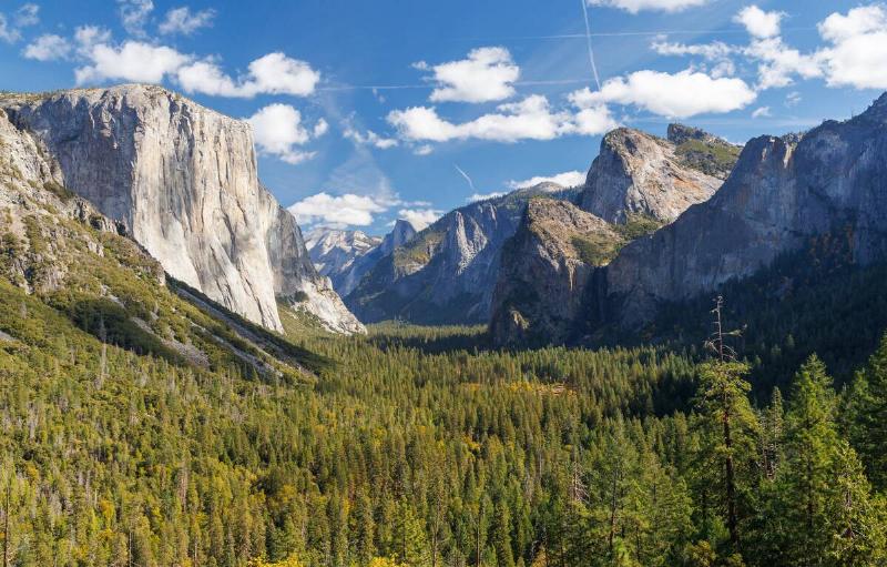 The breathtaking Tunnel View in Yosemite National Park showcases a panoramic vista of El Capitan, Half Dome, and Bridalveil Fall, surrounded by towering granite cliffs and lush forests