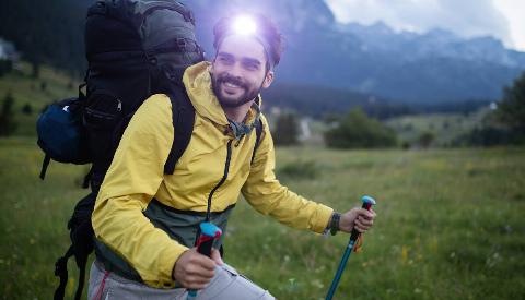 Attractive hiker with big traveling rucksack moving up on the mountain, happy traveler overcome big way smiling looking away, adventure travel and discovery