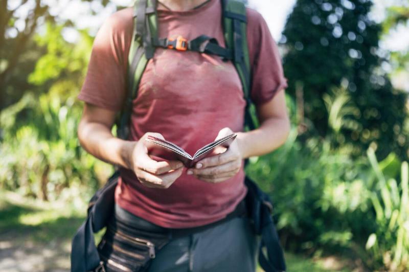 Man in the forest with a small guidebook in his hands.