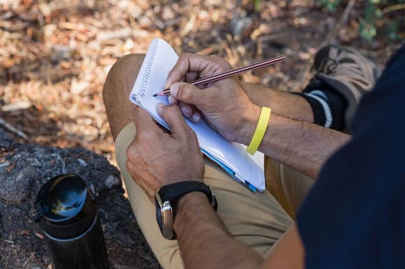 Man writing on notepad while resting on tree trunk in the forest