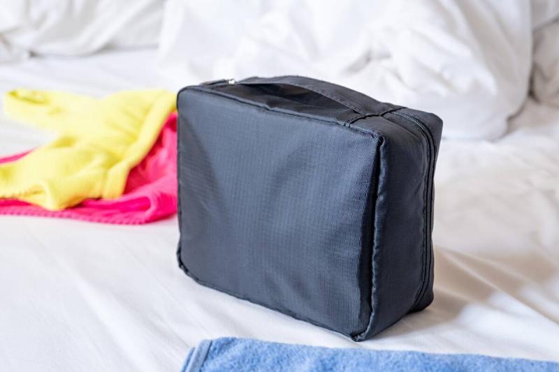 Travel cosmetics kit with bottles, pills and cosmetics on bed.