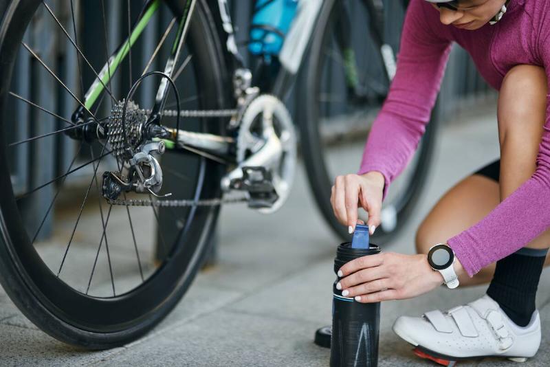 Cropped shot of young woman, professional female cyclist taking pump for inflating the tire of her bicycle, kneeling outdoors on a daytime.