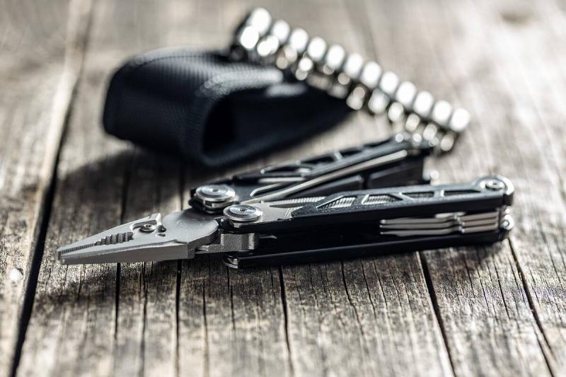 Multi-tools pliers with other tools and knife. Multifunction pliers on wooden table.