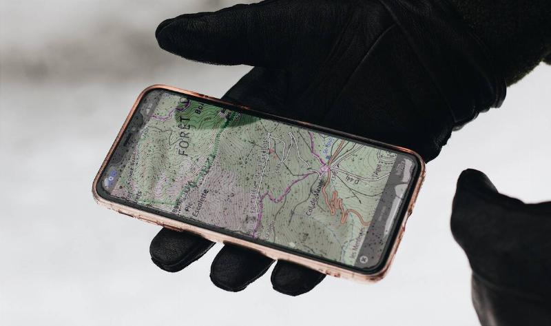 A gloved hand holding a phone with a gps app up.