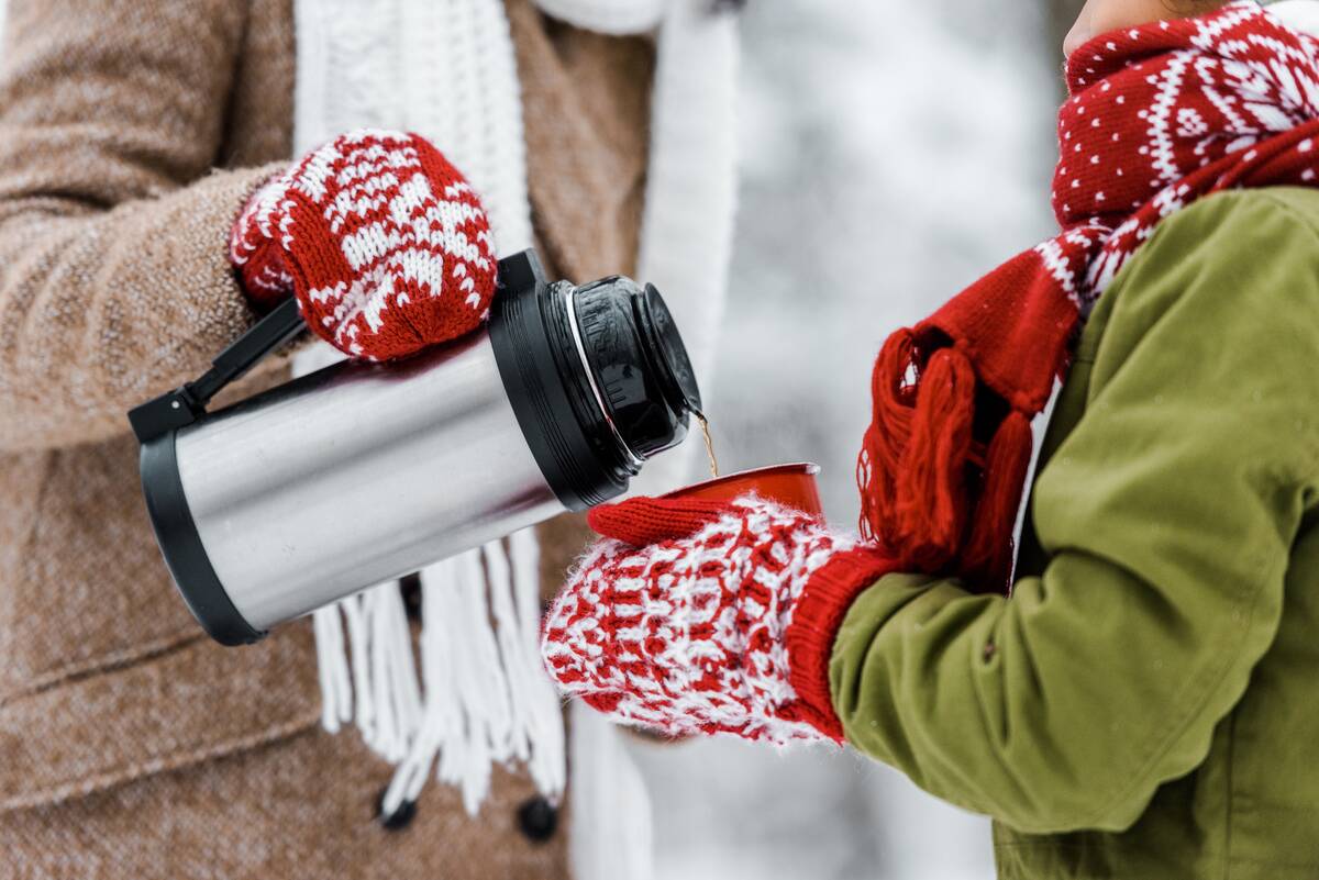 cropped view of woman pouring tea from thermos in red cup holding by child in winter