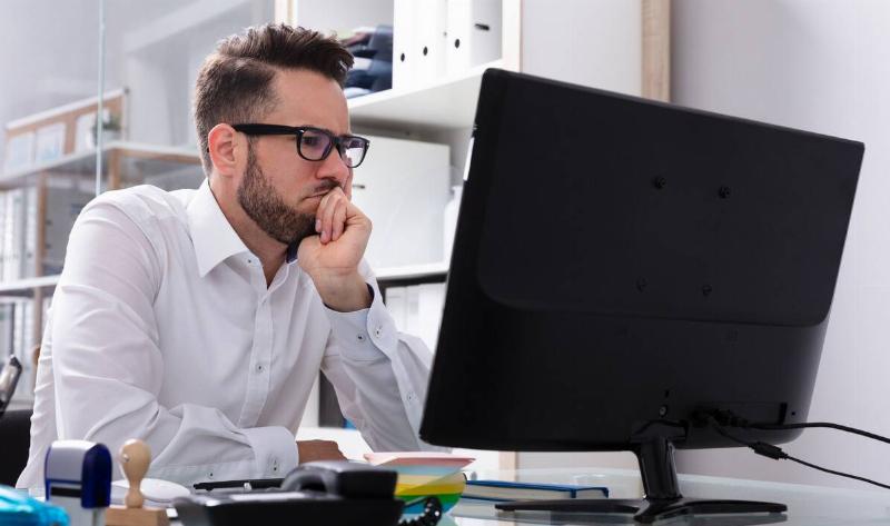 A man sitting at a computer, sporting a thinking expression.