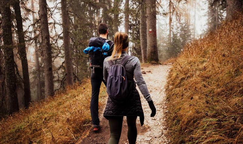 Two people walking a forest trail, both in long clothing.