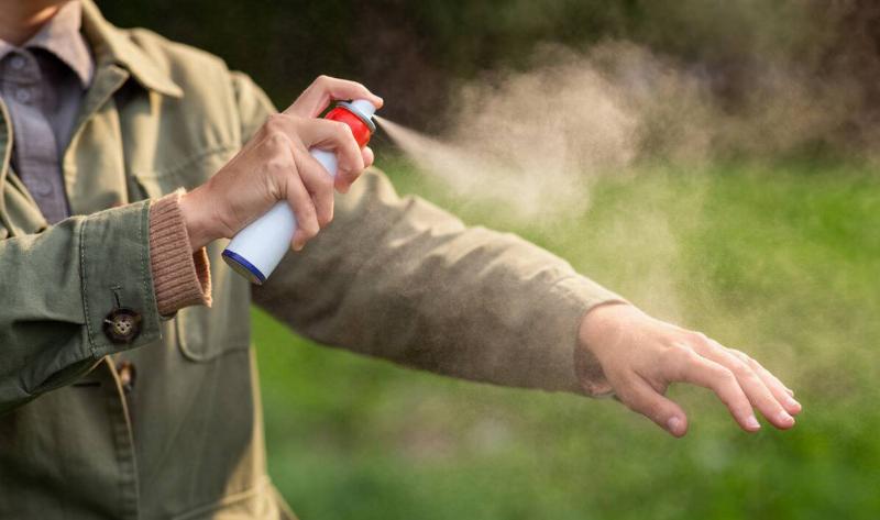 A person spraying themselves with a nondescript bug repellent.