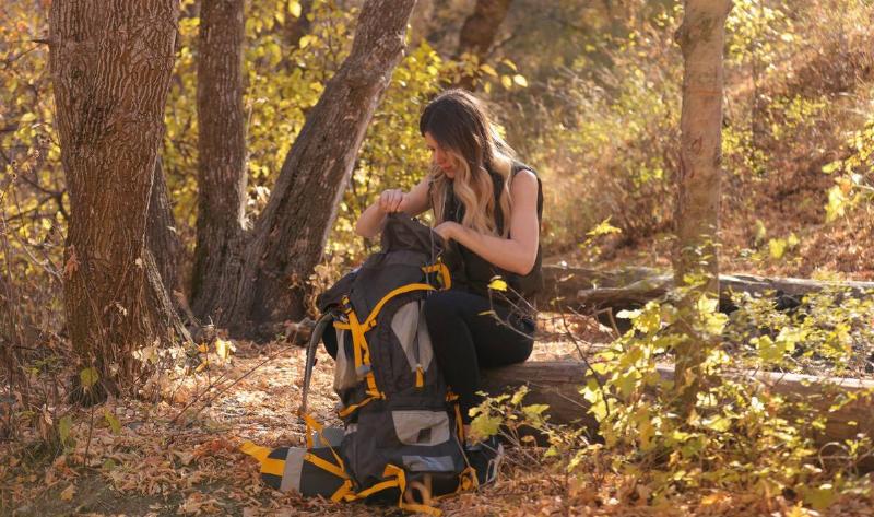 A woman sitting on a log in the woods, looking through her backpack.