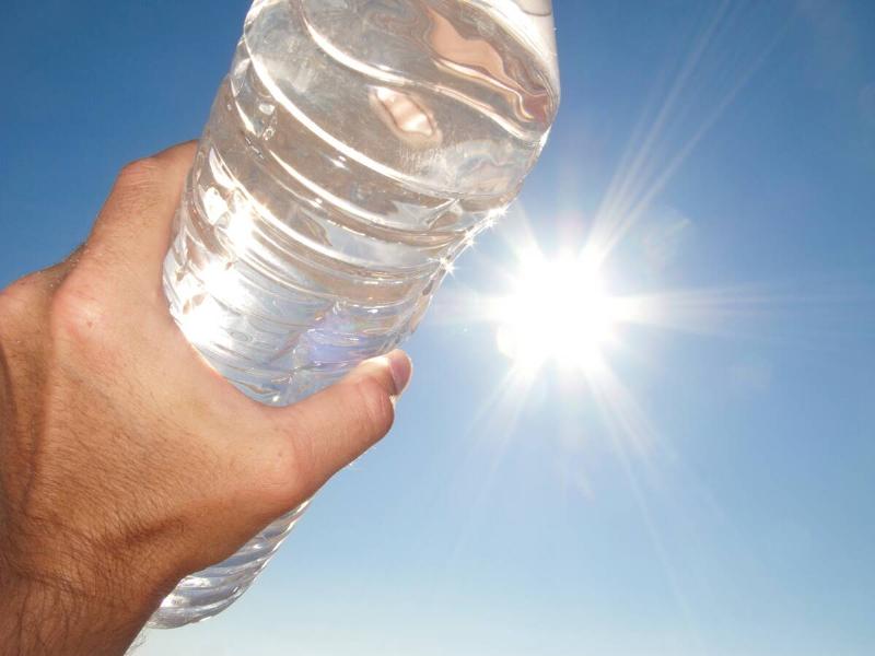 A hand holding a clear plastic water bottle up to the sunshine.