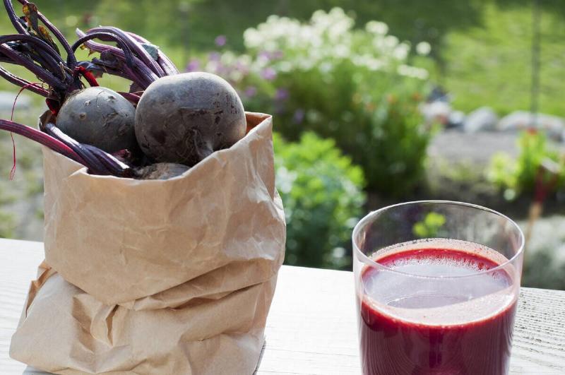 Fresh beetroots in a paper bag next to a glass of beet juice with a garden view.