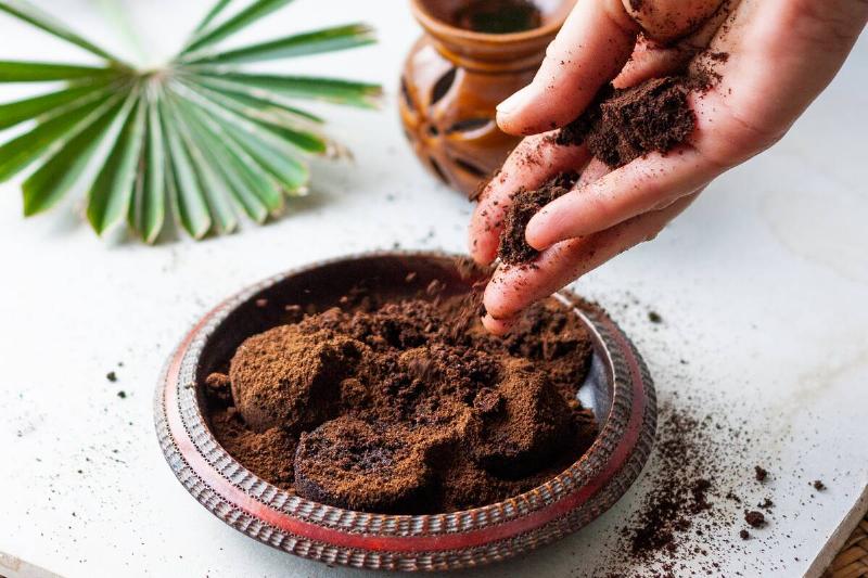 Woman's hand crumbles coffee grounds into wooden bowl. Coffee grounds used as a body scrub or fertilizer for plants.