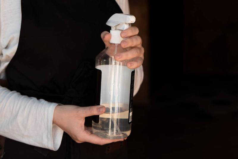 A torso shot of someone holing up a spray bottle with a clear liquid inside.